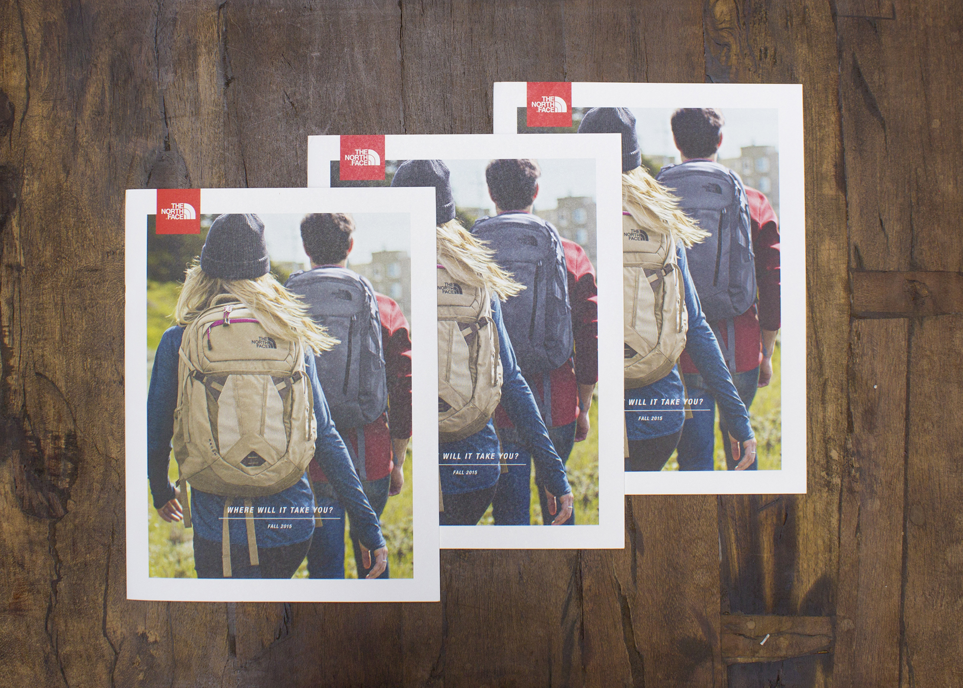 Three copies of The North Face catalog on a wood surface