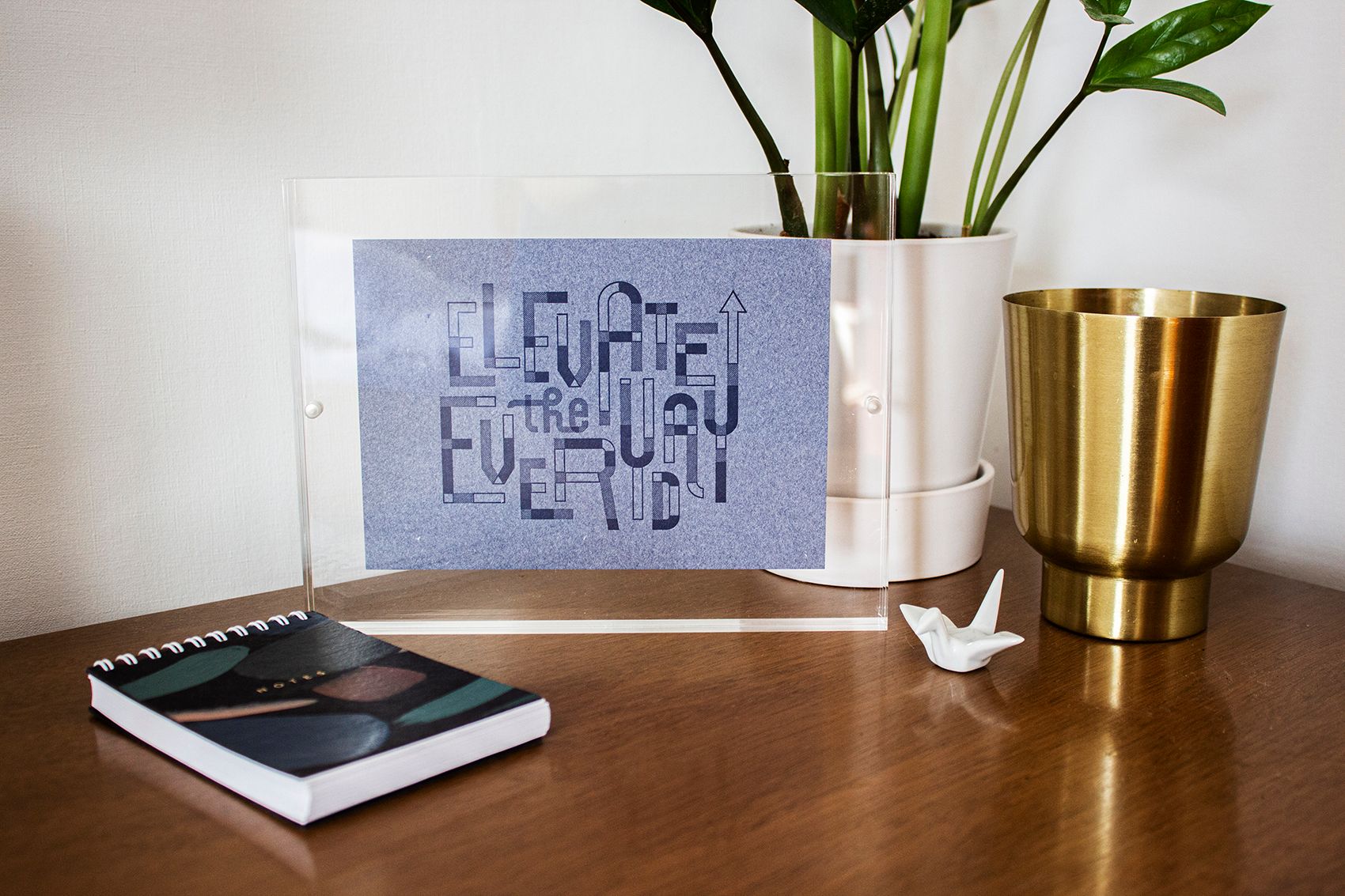 Elevate the Everyday card framed in an acrylic frame and styled next to a plant and notebook